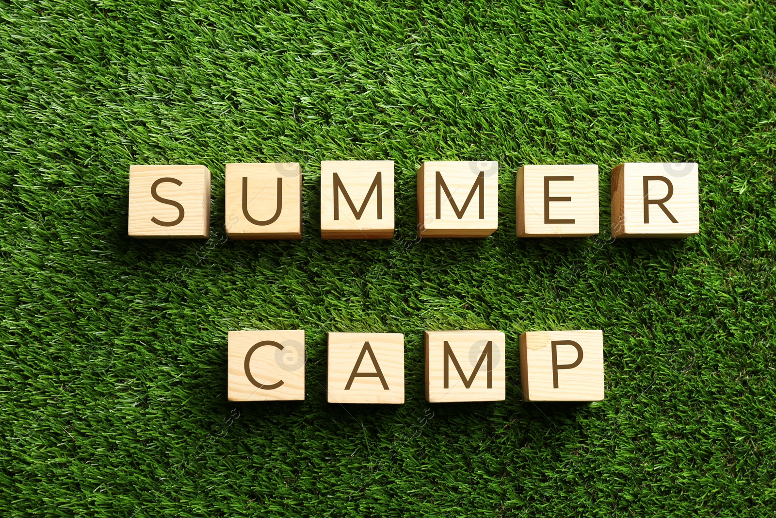 Photo of Phrase SUMMER CAMP made with cubes on green grass, flat lay