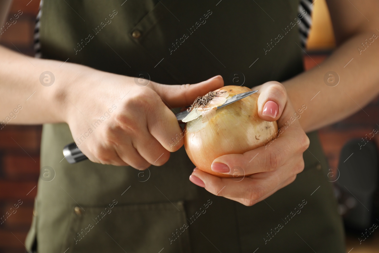Photo of Woman peeling fresh onion with knife indoors, closeup
