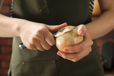 Woman peeling fresh onion with knife indoors, closeup