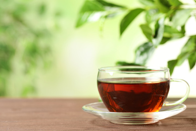 Photo of Cup of black tea on wooden table against blurred background. Space for text