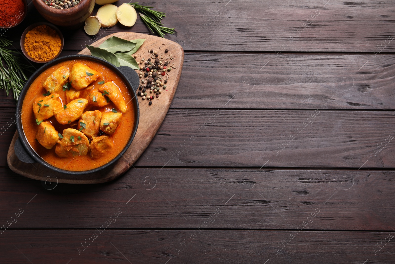 Photo of Delicious chicken curry in pan on wooden table, flat lay. Space for text