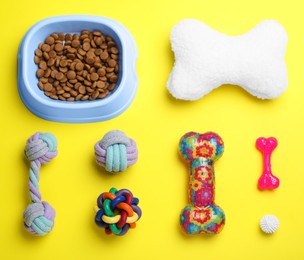 Photo of Feeding bowl and toys for pet on yellow background, flat lay