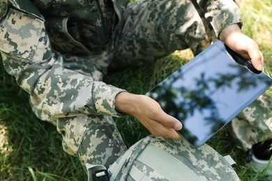 Photo of Soldier with backpack using tablet near tree in forest, closeup
