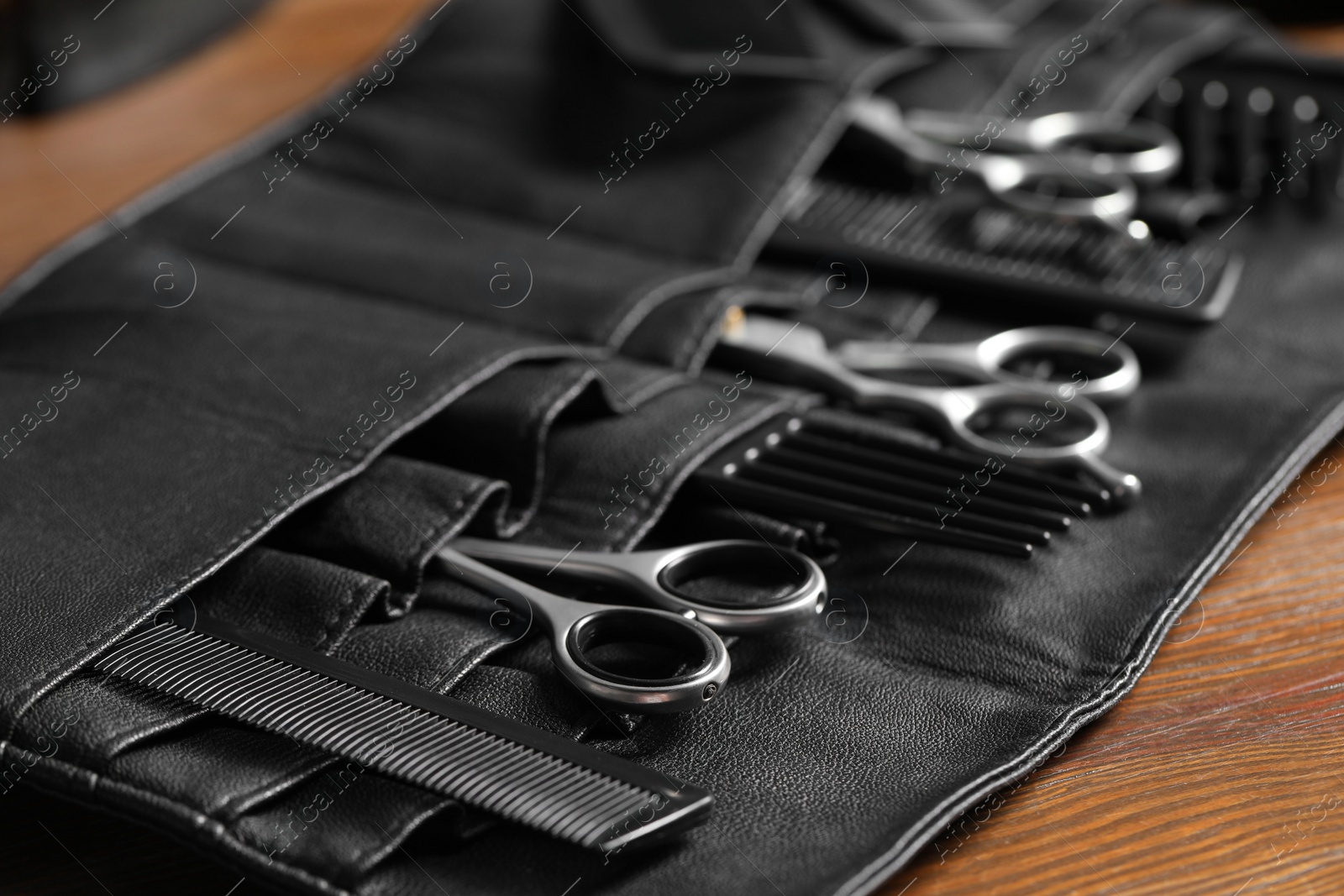 Photo of Hairdresser tools. Professional scissors and combs in leather organizer on wooden table, closeup