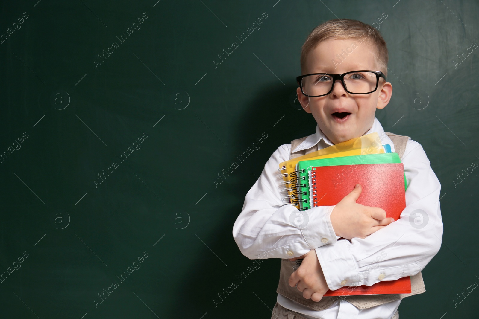 Photo of Cute little child wearing glasses near chalkboard, space for text. First time at school