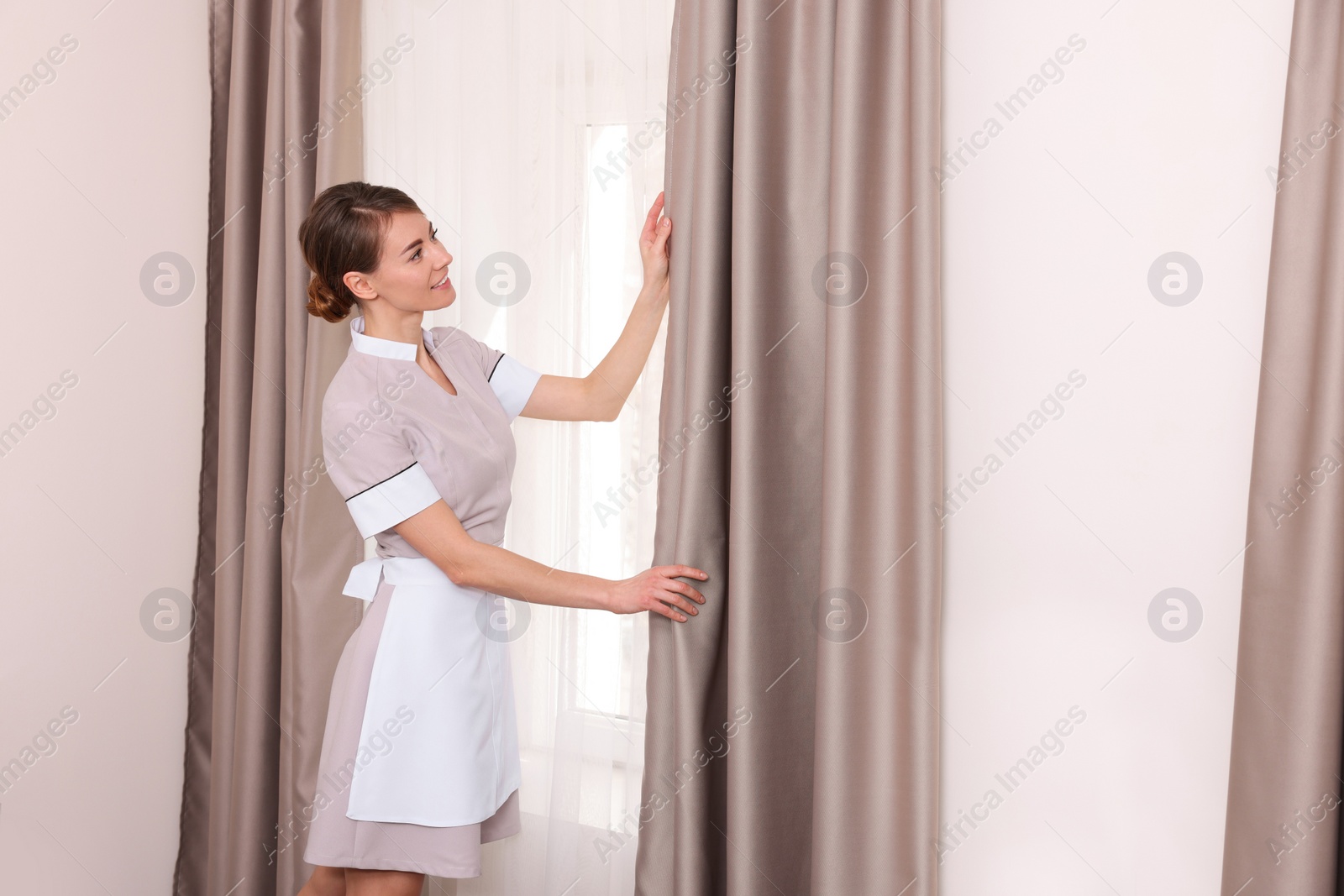 Photo of Beautiful chambermaid opening window curtains in hotel room