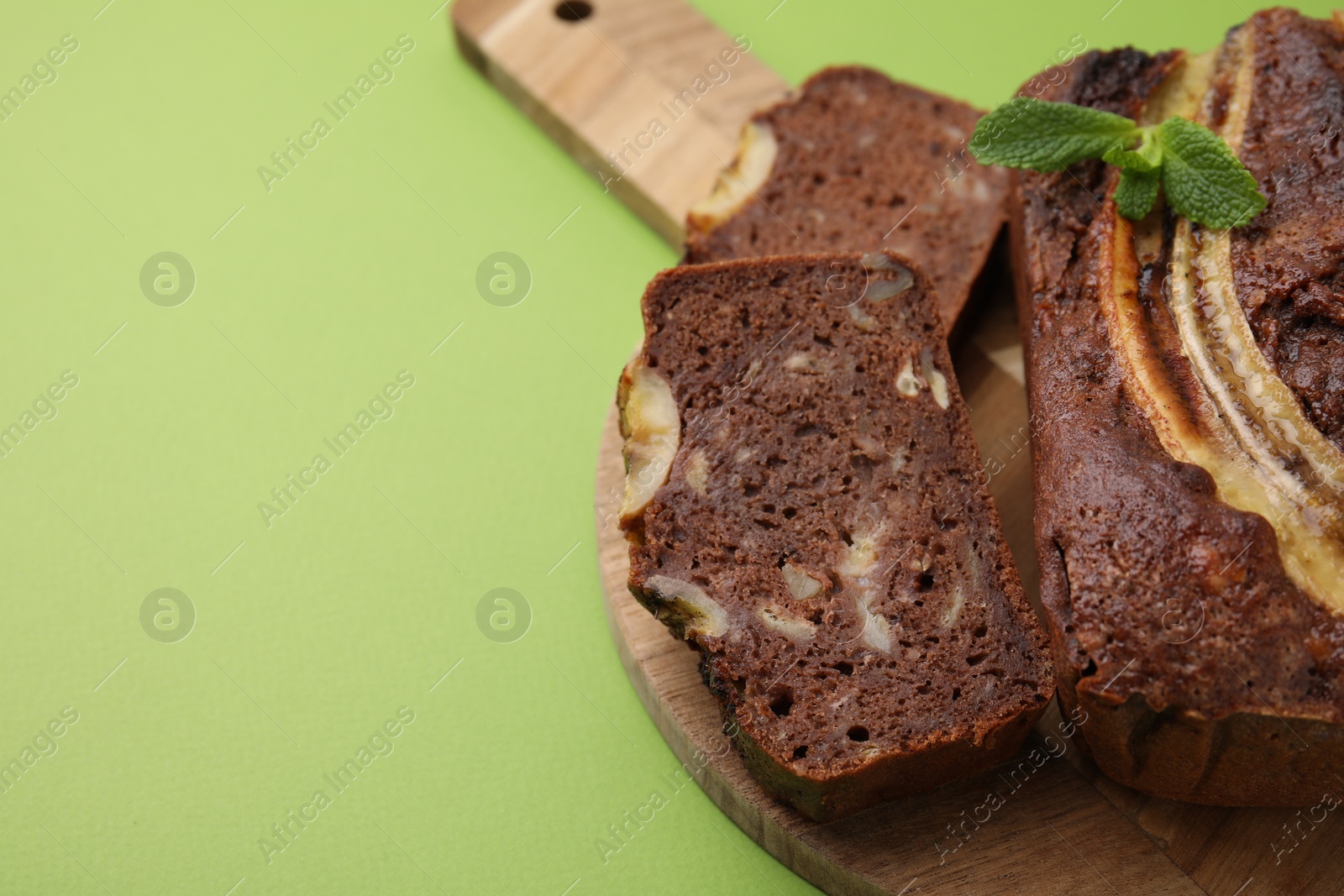 Photo of Delicious banana bread with mint on green background, closeup. Space for text