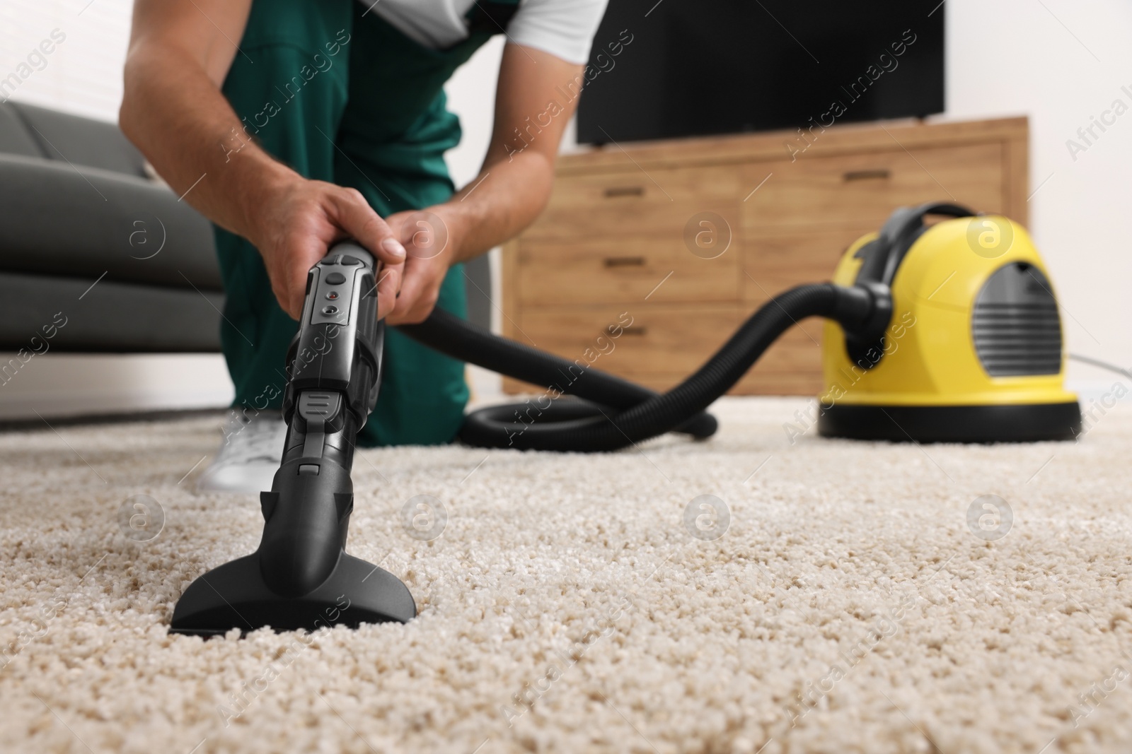 Photo of Dry cleaner's employee hoovering carpet with vacuum cleaner indoors, closeup. Space for text