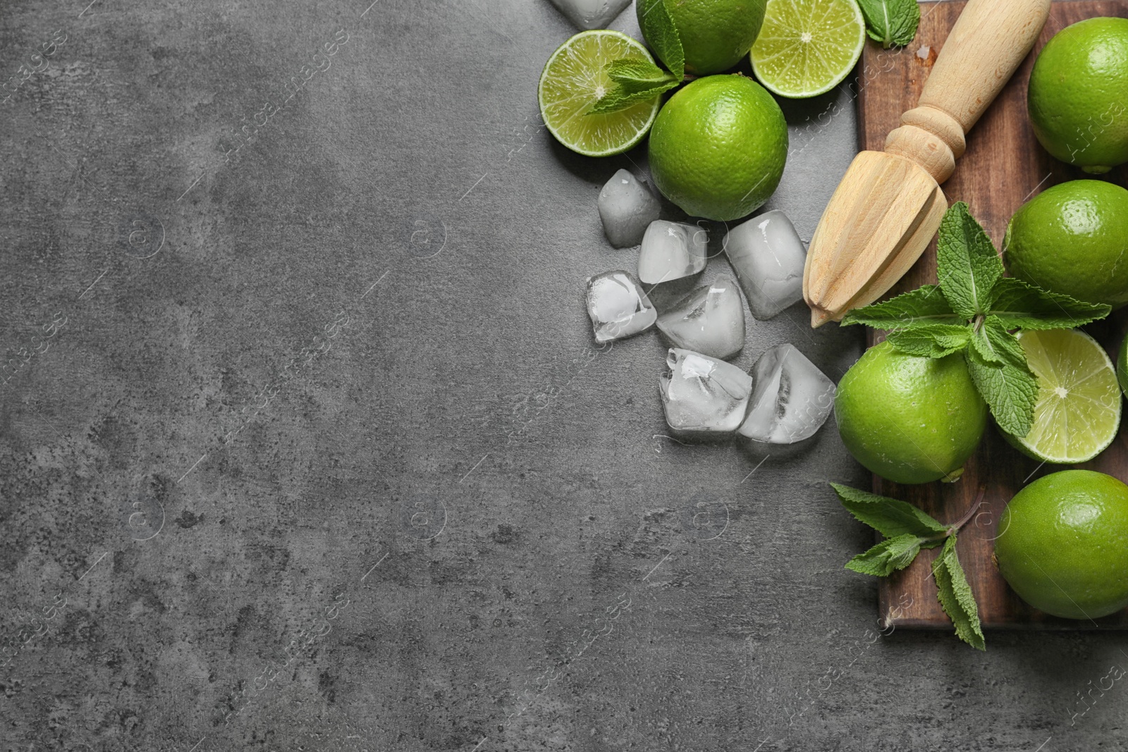 Photo of Flat lay composition with ripe limes, ice cubes and juicer on grey background. Refreshing beverage recipe