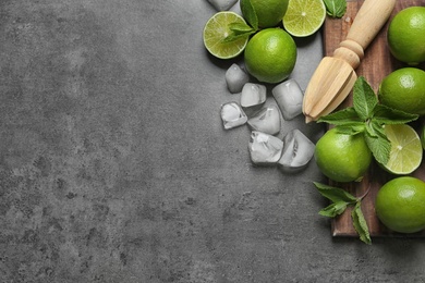 Flat lay composition with ripe limes, ice cubes and juicer on grey background. Refreshing beverage recipe