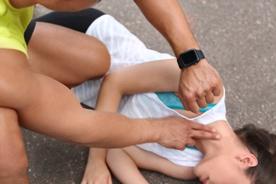 Photo of Young man checking pulse of unconscious woman on street, closeup