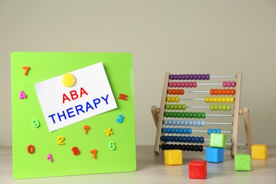 Photo of Magnetic board with phrase ABA Therapy, colorful numbers and abacus on white wooden table