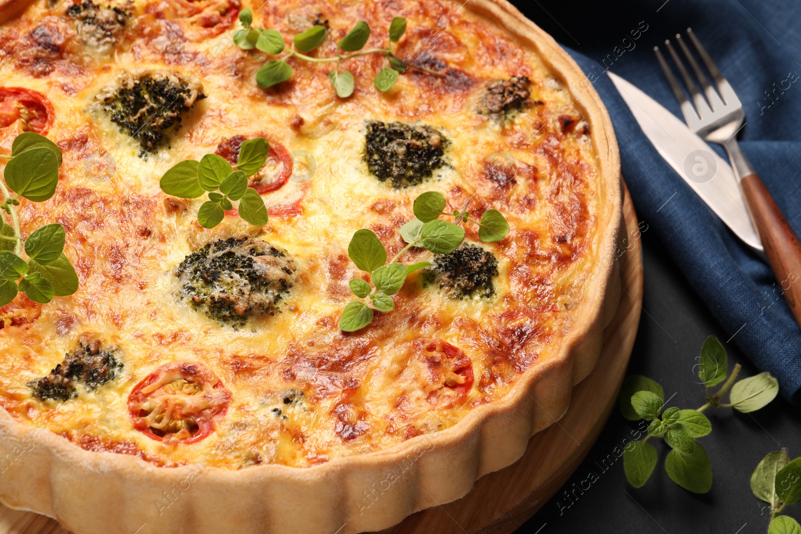 Photo of Delicious homemade vegetable quiche and oregano on dark table, closeup