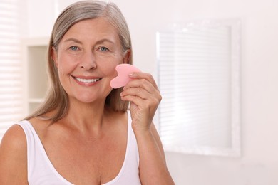 Photo of Woman massaging her face with rose quartz gua sha tool in bathroom. Space for text