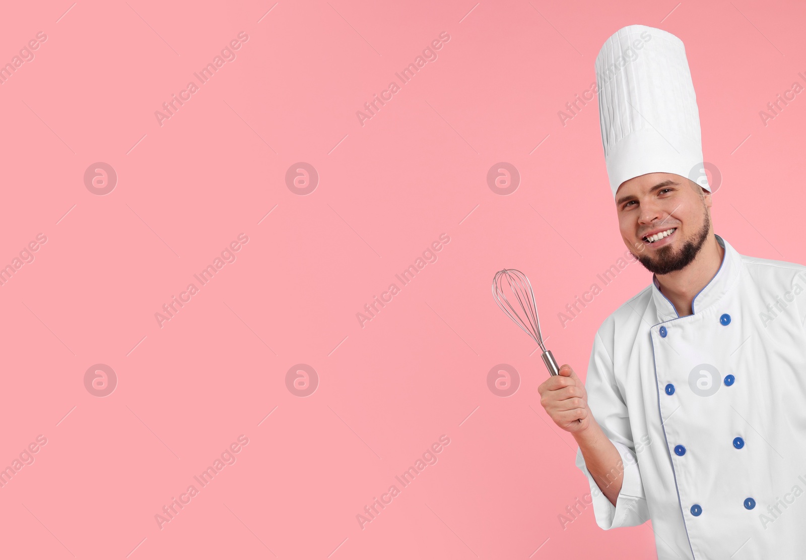 Photo of Happy professional confectioner in uniform holding whisk on pink background. Space for text