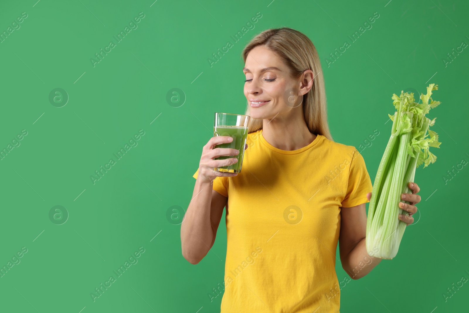 Photo of Happy woman with glass of tasty celery juice and fresh vegetable on green background. Space for text