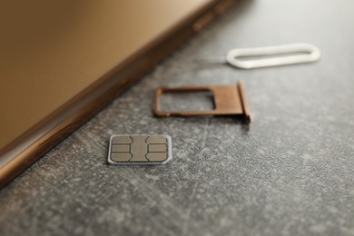 Photo of SIM card, mobile phone, tray and ejector tool on grey table, closeup