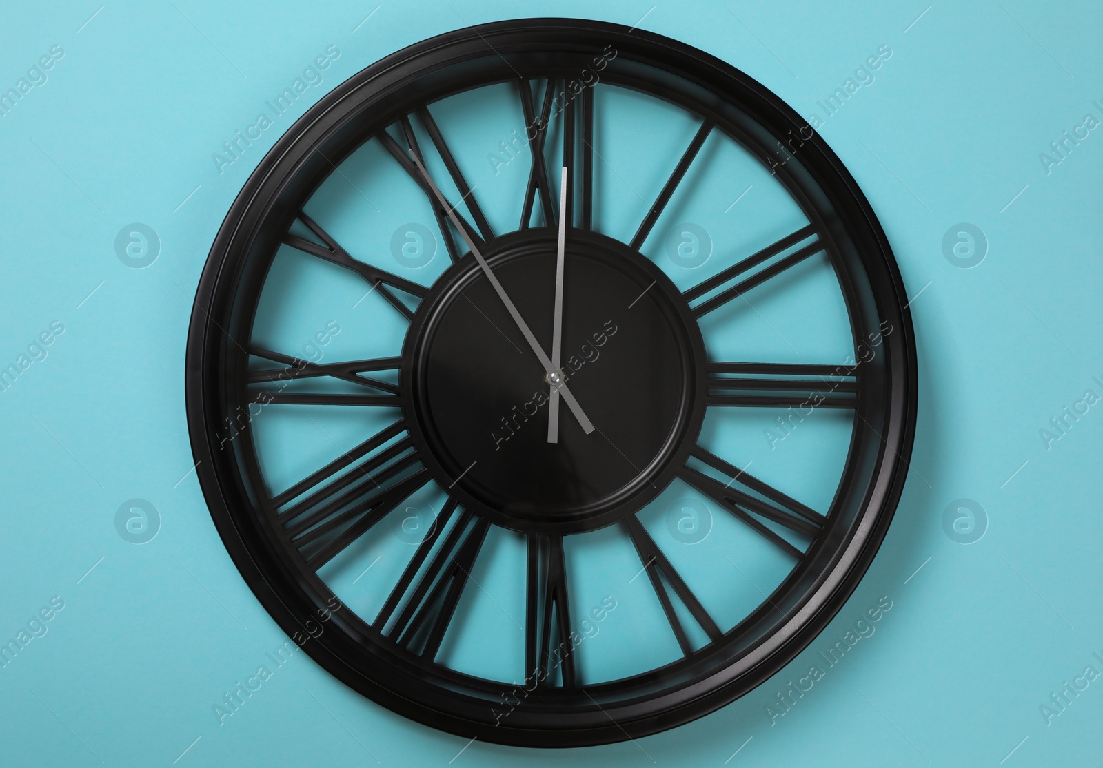 Photo of Stylish analog clock hanging on light blue wall. New Year countdown