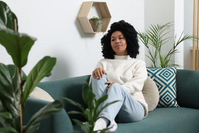 Relaxing atmosphere. Woman sitting on sofa near beautiful houseplants at home