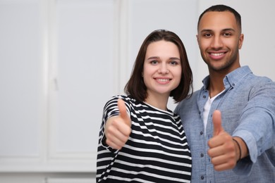 Dating agency. Happy couple showing thumbs up near white wall, space for text