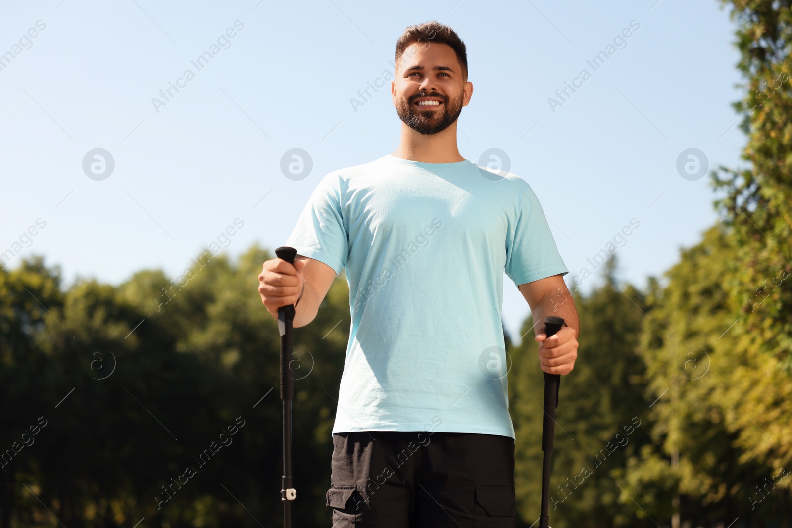 Photo of Happy man practicing Nordic walking with poles outdoors on sunny day