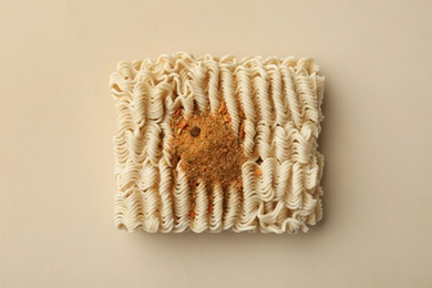 Block of quick cooking noodles with spices on color background, top view