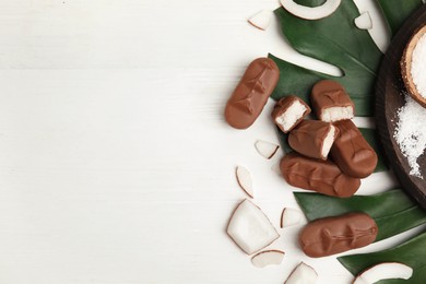 Delicious milk chocolate candy bars with coconut filling on white wooden table, flat lay. Space for text