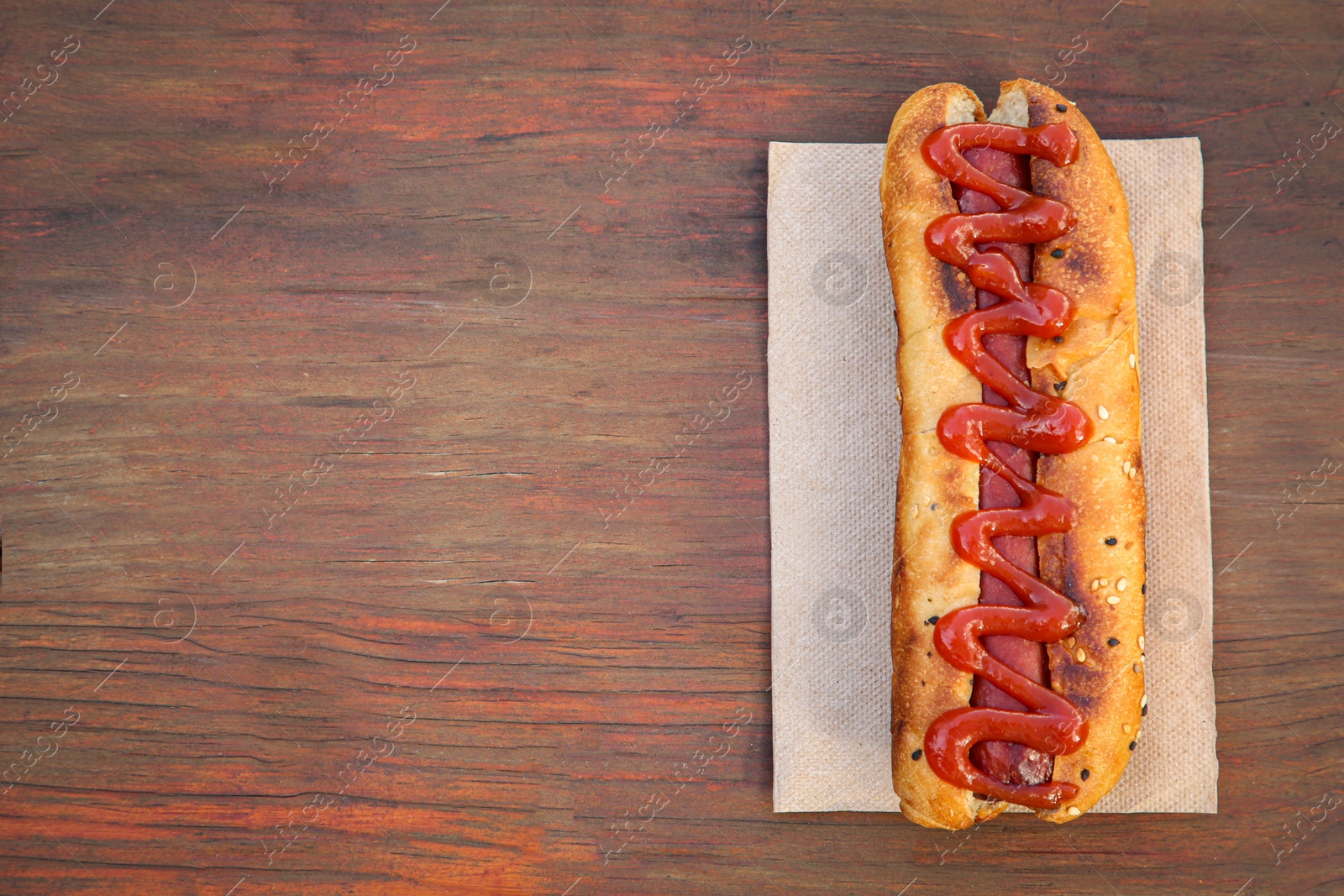 Photo of Fresh tasty hot dog with ketchup on wooden table, top view. Space for text