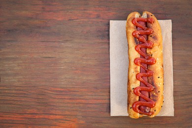 Photo of Fresh tasty hot dog with ketchup on wooden table, top view. Space for text