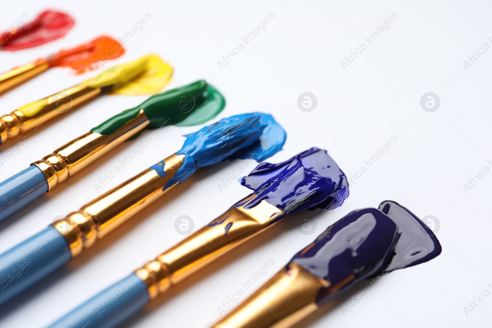 Photo of Set of brushes with different paints on white background, closeup. Rainbow colors