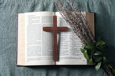 Bible, wooden cross and bouquet with willow branches on color cloth, flat lay