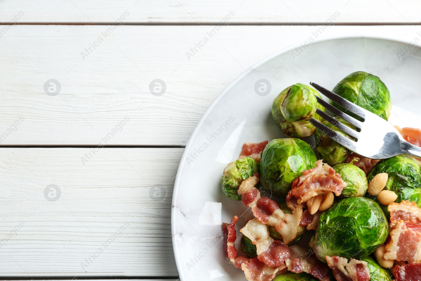 Photo of Delicious Brussels sprouts with bacon on white wooden table, top view. Space for text