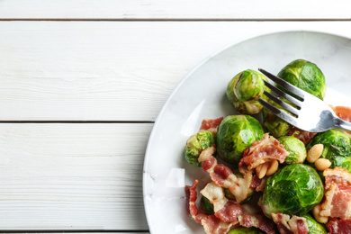 Photo of Delicious Brussels sprouts with bacon on white wooden table, top view. Space for text