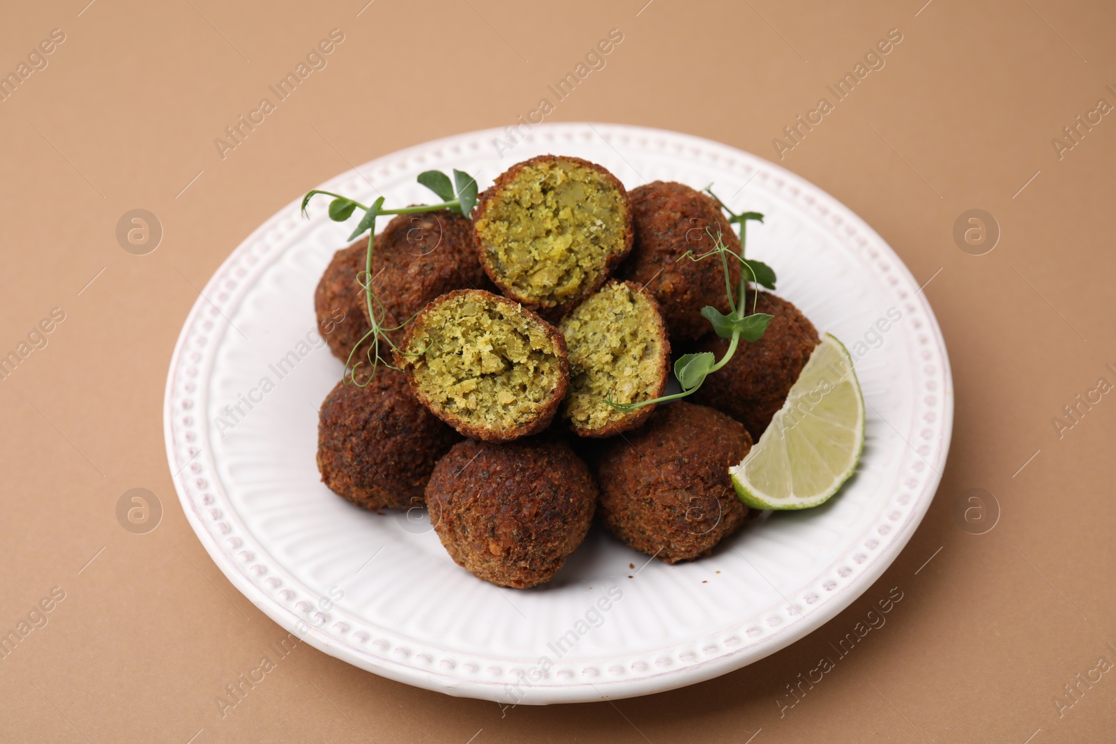 Photo of Delicious falafel balls, lime slice and microgreens on pale brown background