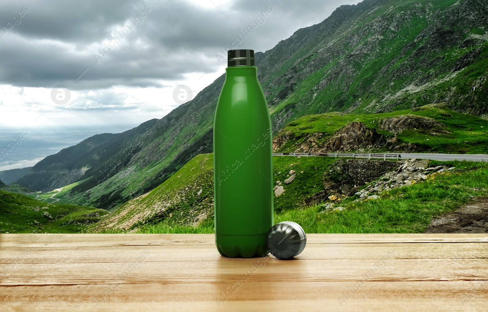Image of Wooden desk with thermo bottle and mountain landscape on background
