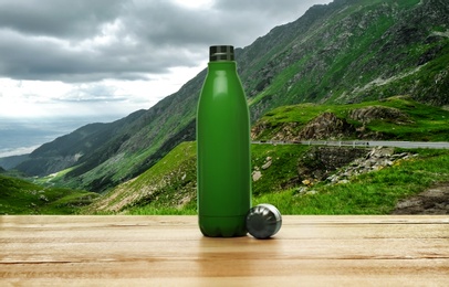 Image of Wooden desk with thermo bottle and mountain landscape on background