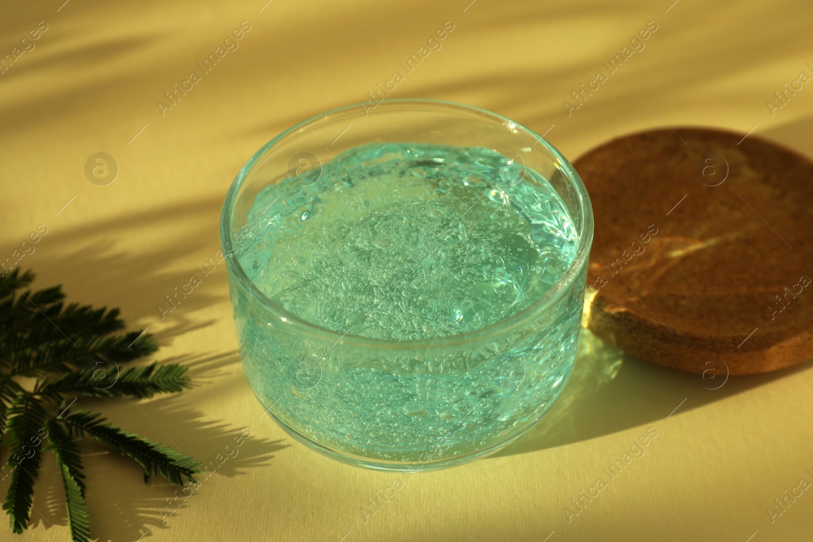 Photo of Jar of cosmetic gel and leaves on yellow background