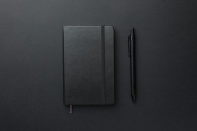 Closed notebook and pen on black background, top view