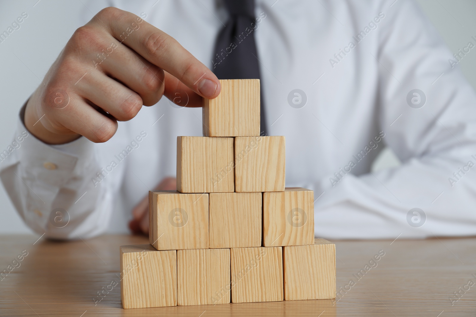 Photo of Businessman building pyramid of blank cubes on wooden table, closeup. Space for text