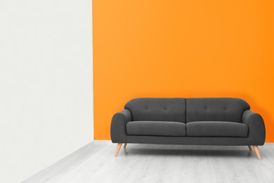 Photo of Stylish room with cosy sofa near orange wall, space for text. Interior design
