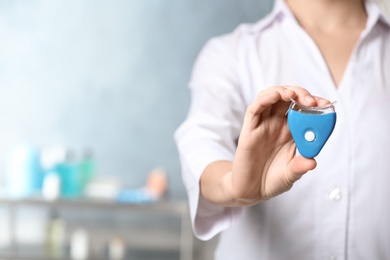 Photo of Female dentist holding teeth whitening device on blurred background, space for text