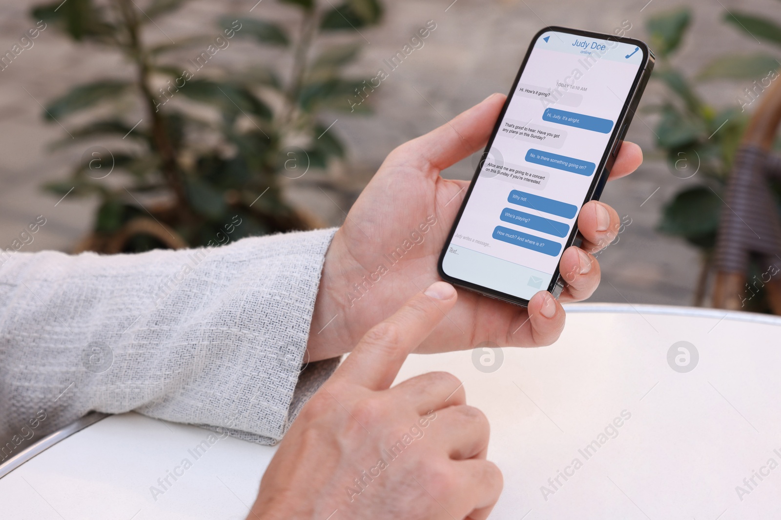 Image of Man texting via mobile phone at table outdoors, closeup. Device screen with messages