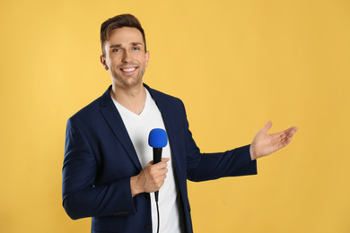 Young male journalist with microphone on yellow background