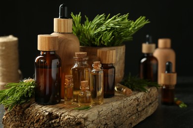 Photo of Essential oils in bottles, rosemary and wood on table against black background, closeup