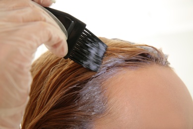 Young woman applying hair dye on roots against light background, closeup