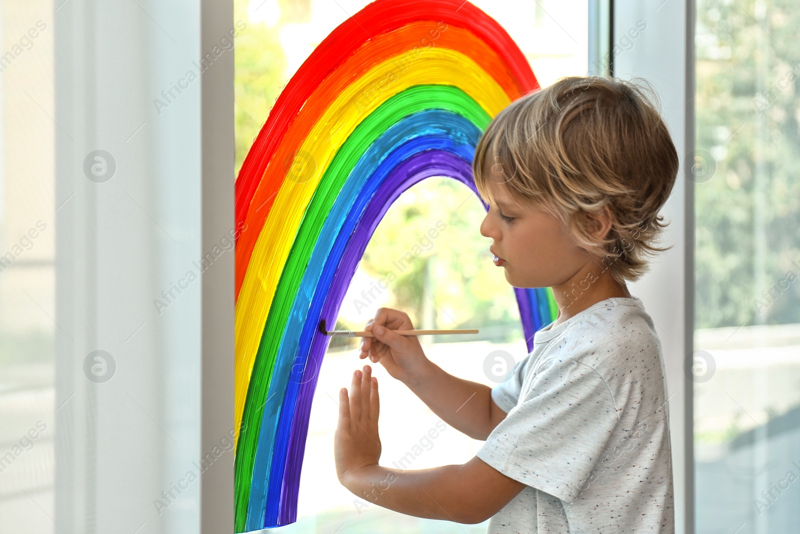 Photo of Little boy drawing rainbow on window. Stay at home concept