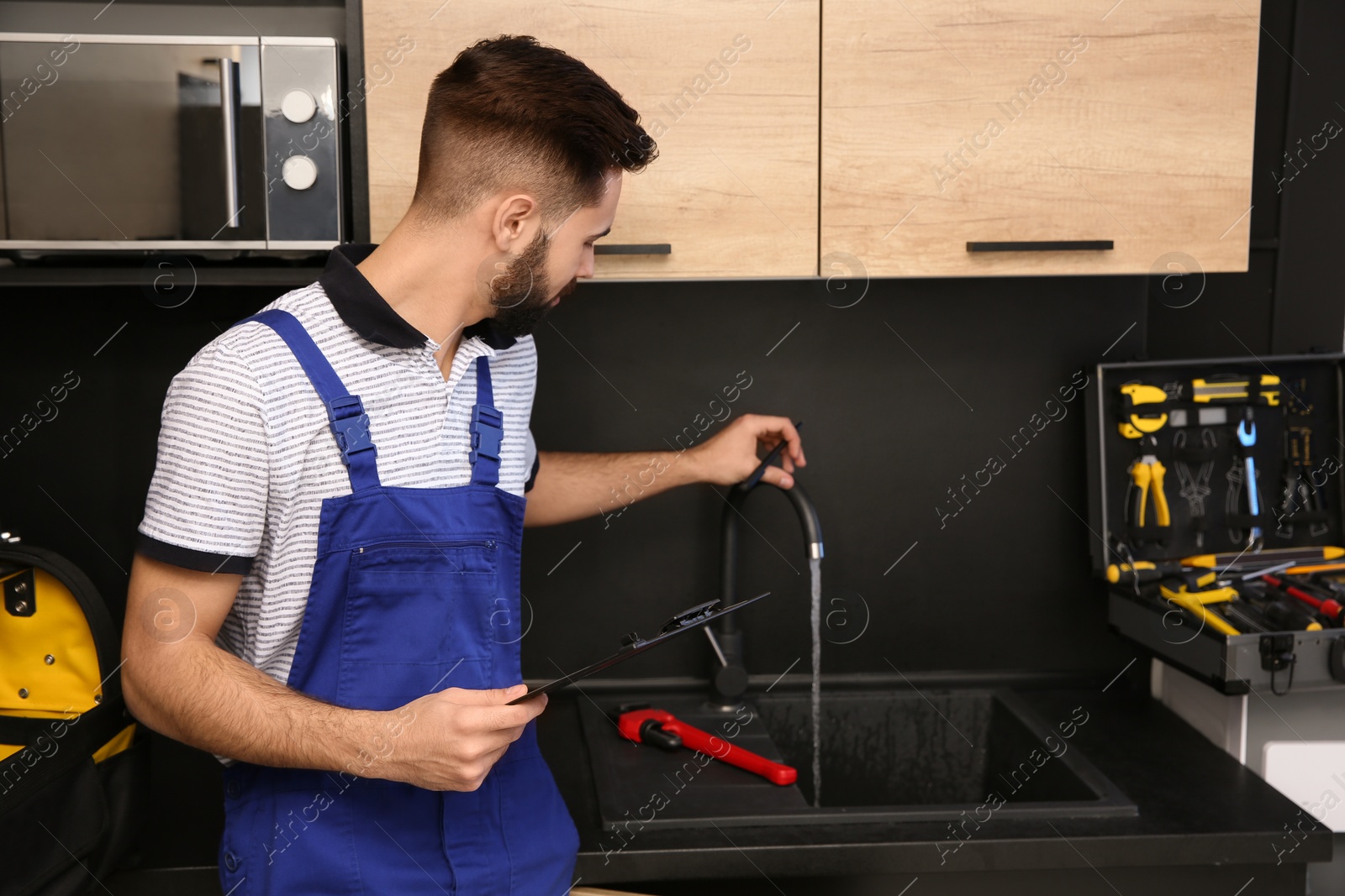 Photo of Male plumber in uniform checking faucet in kitchen. Repair service