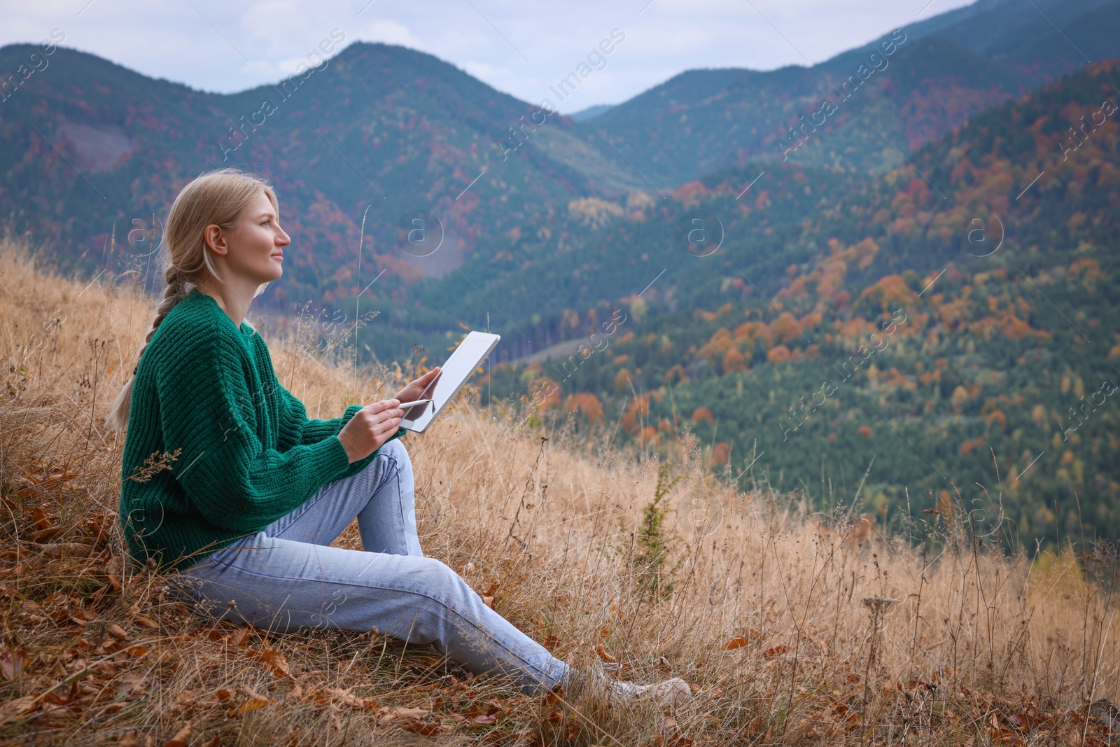 Photo of Young woman drawing on tablet in mountains