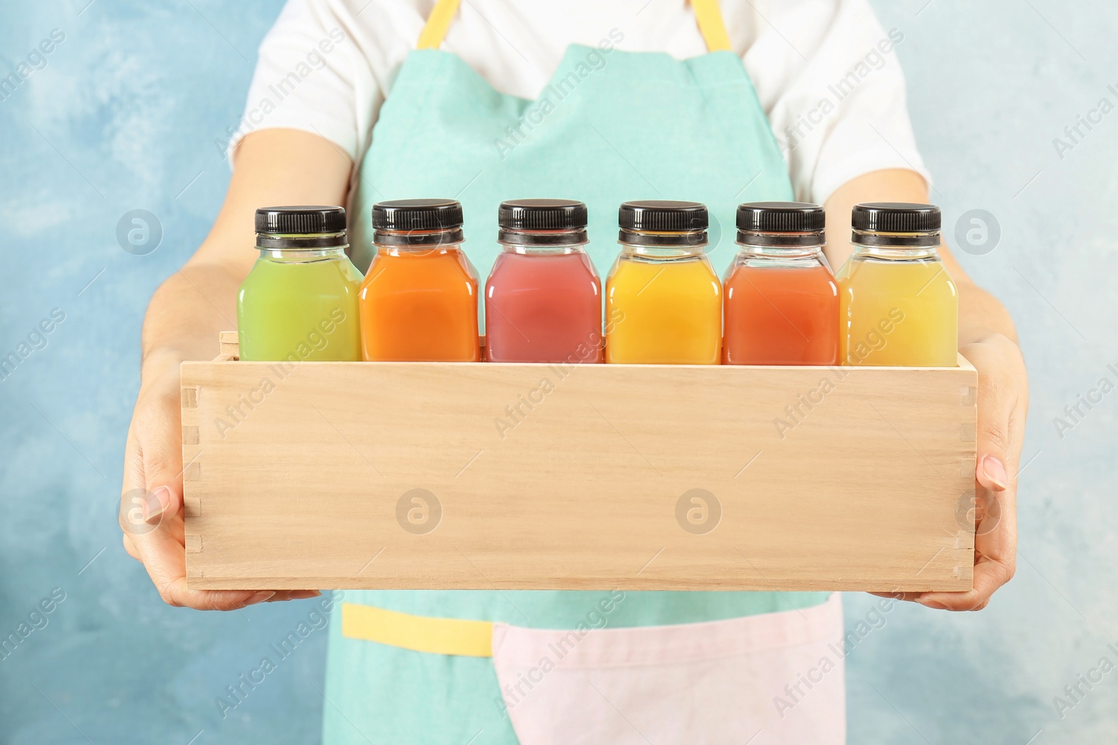 Photo of Woman holding wooden crate with tasty juices on color background