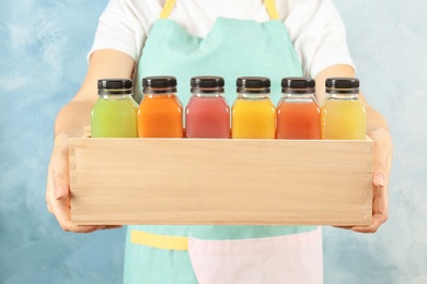 Woman holding wooden crate with tasty juices on color background